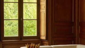A room with a large window, a beige sofa, a wooden coffee table, and a vase with dried flowers. - Exquisite Château de Thauvenay surrounded by Sancerre vineyards, 24 beds 23bath  (Thauvenay)