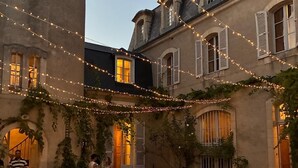 An outdoor dining area with string lights, tables set for a meal, and a building with arched windows and shutters. - Exquisite Château de Thauvenay surrounded by Sancerre vineyards, 24 beds 23bath  (Thauvenay)