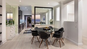 A modern dining area with a glass table, black chairs, and a view of the ocean through a large window. - YOLO Spaces Clifton - Clifton Beachfront Magic Apartment (Cape Town)