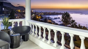 A balcony with a white balustrade overlooking a coastal town at dusk. - YOLO Spaces Clifton - Clifton Beachfront Magic Apartment (Cape Town)