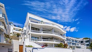 A modern multi-story hotel with balconies, a curved facade, and a clear blue sky. - YOLO Spaces Clifton - Clifton Beachfront Magic Apartment (Cape Town)