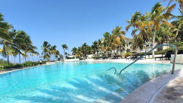 A clear blue pool surrounded by palm trees and lounge chairs. - Condominio Aquamarina (Punta Cana)