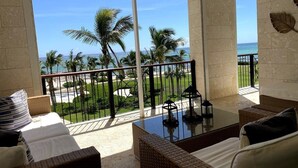 A balcony with wicker furniture, a glass table, and a view of the beach and palm trees. - Condominio Aquamarina (Punta Cana)