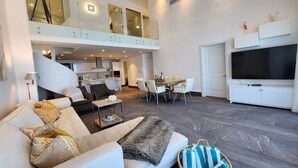 A spacious living area with a high ceiling, a balcony, a dining area, and a TV. - Condominio Aquamarina (Punta Cana)