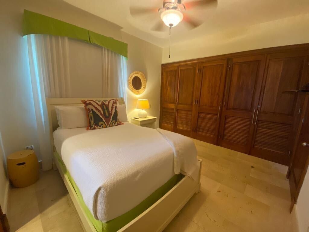 A bedroom with a bed, a nightstand, a lamp, a ceiling fan, and a wardrobe.