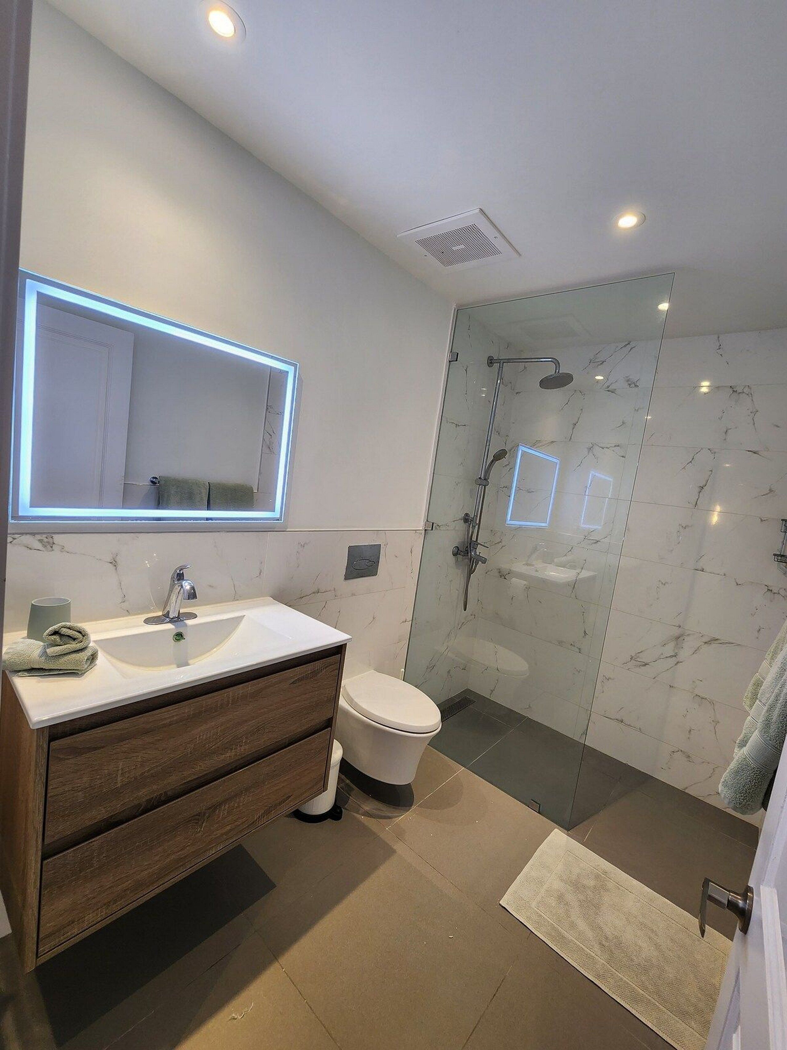 A modern bathroom with a marble sink, a glass shower enclosure, and a toilet.