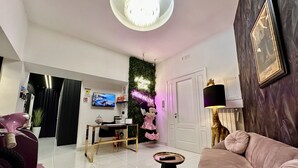 A modern living room with a pink sofa, a small round table, a television, and a decorative wall with greenery and a neon sign. - Elegance Rooms Spaccanapoli (Naples)