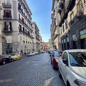 Une rue pavée bordée d’immeubles à plusieurs étages, dont certains sont dotés de balcons et d’antennes paraboliques.