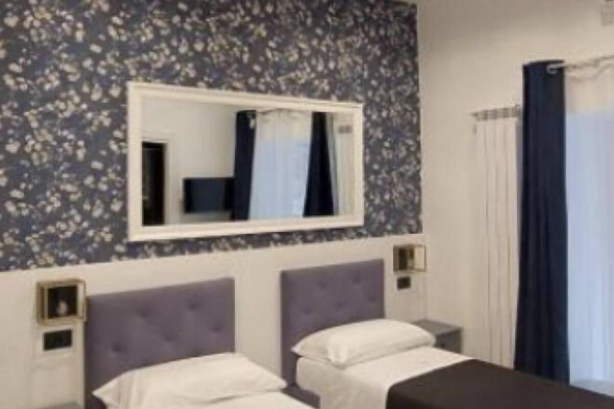 Une chambre d’hôtel avec deux lits, un grand miroir et une fenêtre avec des rideaux.