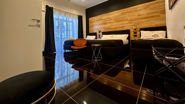 A modern hotel room with a black and white color scheme, a large bed, a small table, a chair, and a view of the outside. - Elegance Rooms Spaccanapoli (Naples)