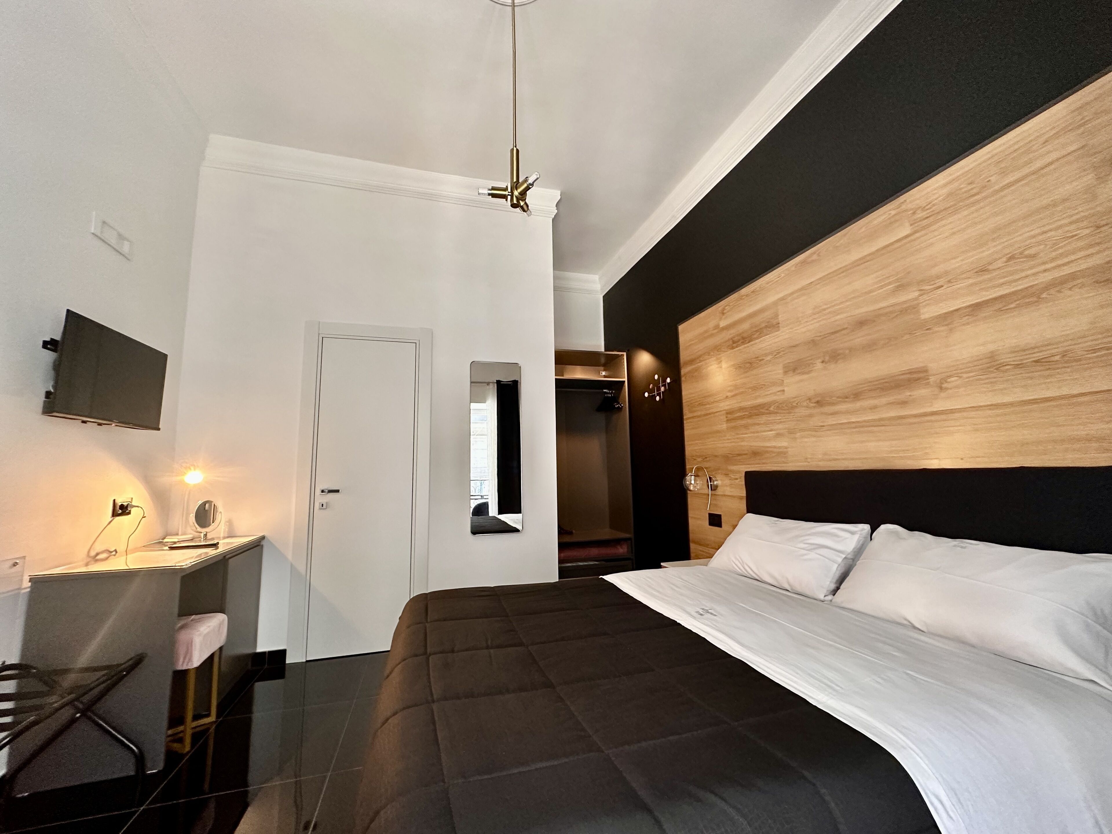 A modern bedroom with a large bed, a desk with a mirror, and a TV mounted on the wall.