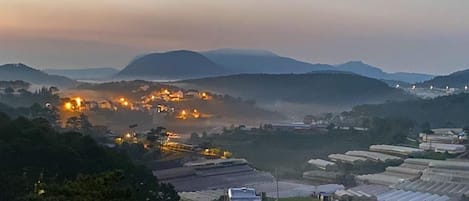 A rural landscape with a village at dusk, featuring illuminated buildings and a mountainous backdrop.