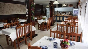 A restaurant with wooden tables and chairs, white tablecloths, and blue and white patterned plates. - Hotel Kima (Bombinhas)