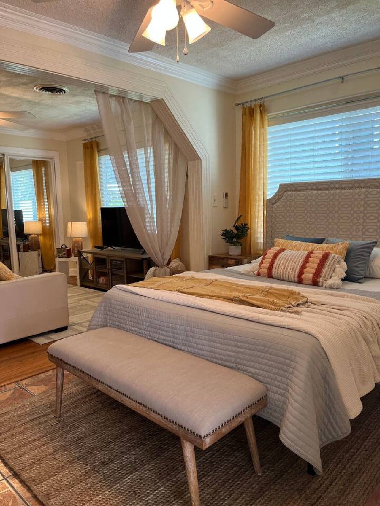 A hotel room with a bed, a bench, a desk, and a television.