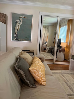 Un salon avec un canapé beige, un tableau encadré représentant un oiseau et un grand miroir qui reflète la pièce.