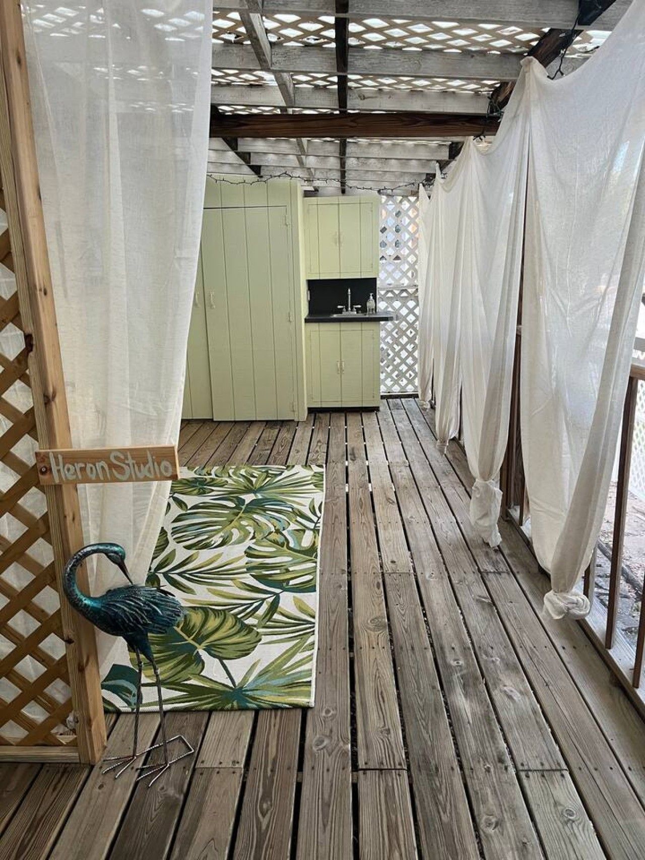 A covered outdoor area with a wooden deck, a small kitchenette, and a decorative bird sculpture.