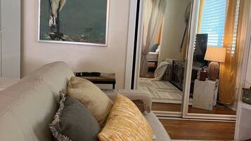 A living room with a beige sofa, a framed painting of a bird, and a large mirror reflecting the room.