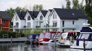 A row of white houses with dark roofs, a dock with small boats, and a calm water body. - Appartement Hafenflair am Plauer See (Plau am See)