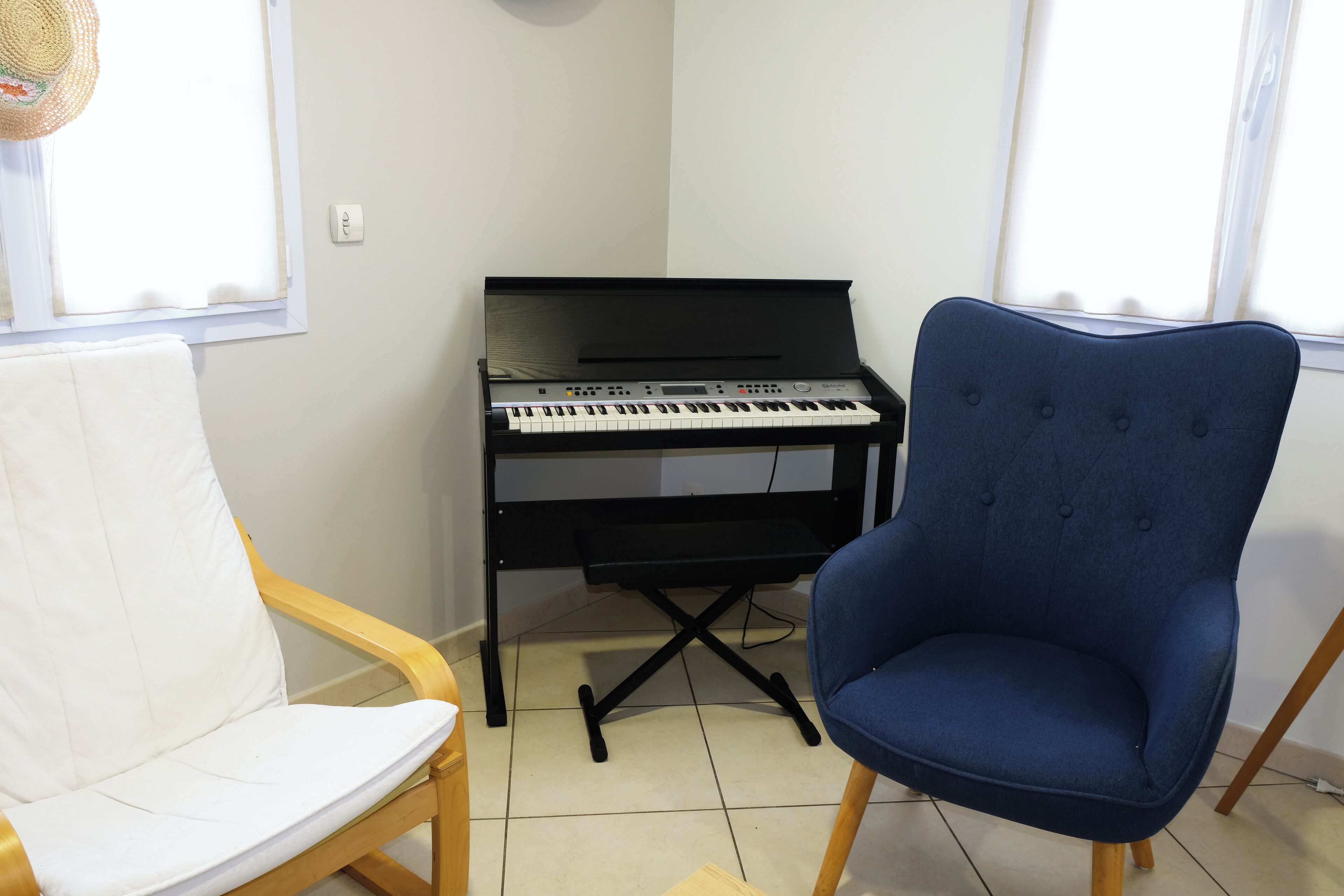 Una habitación con un piano, una silla blanca acolchada y una butaca azul tapizada.
