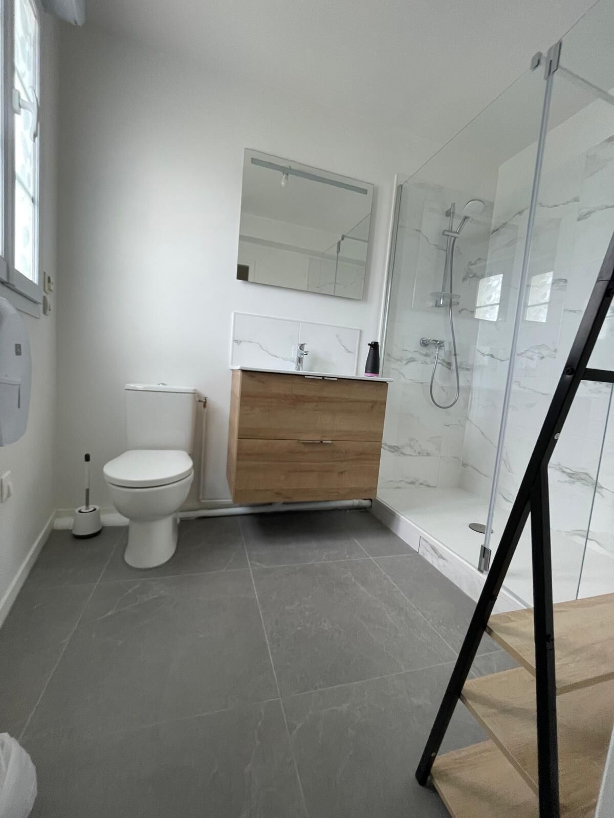 A bathroom with a toilet, a wooden vanity, a mirror, and a glass shower enclosure.