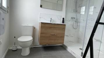 A bathroom with a toilet, a wooden vanity, a mirror, and a glass shower enclosure.