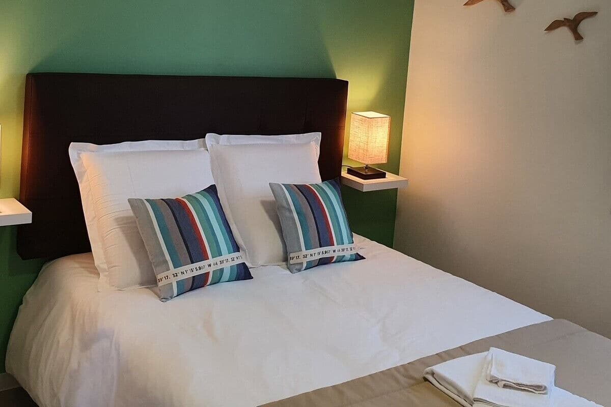 A neatly made bed with white linens and striped pillows, a dark headboard, and a bedside lamp.