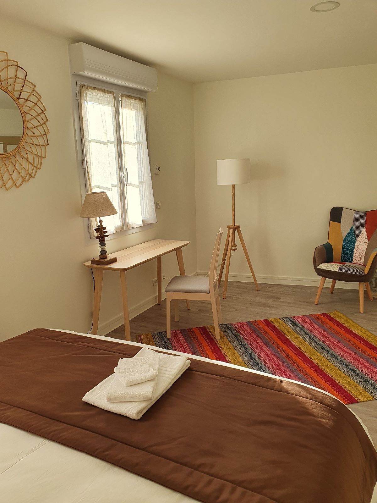 Une chambre à coucher avec un lit, un bureau, une chaise, une lampe sur pied et un tapis coloré.