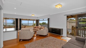 Ein modernes Wohnzimmer mit einer Couch, Sesseln und einem Couchtisch. Ein großes Fenster bietet Blick aufs Meer.