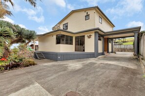 A two-story house with a covered patio and a concrete driveway. - Seaside on Stratford - Cable Bay Holiday Home (Cable Bay)