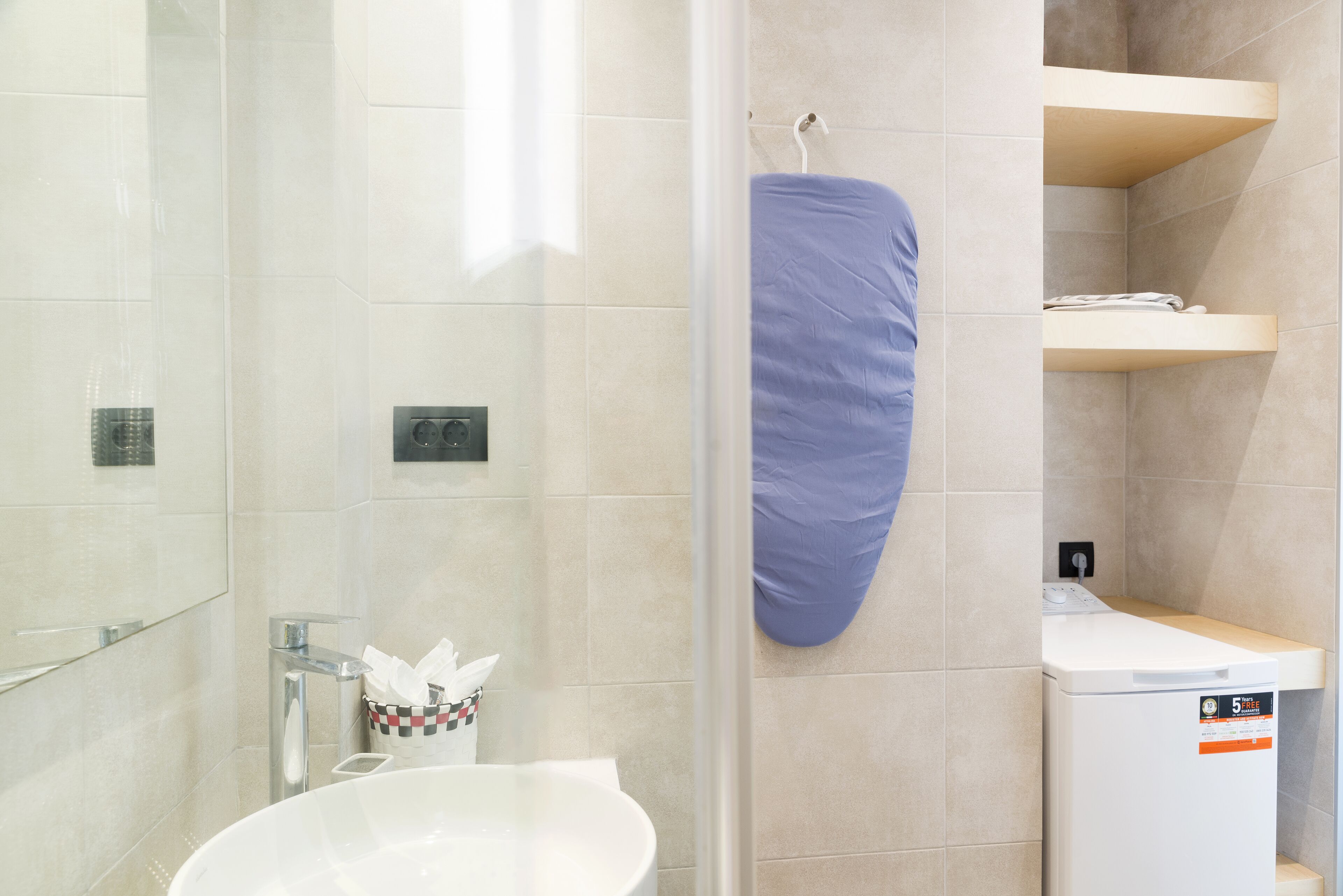 Een moderne badkamer met een douchecabine van glas, een wit wastafelmeubel, een handdoekrek en een wasmachine.