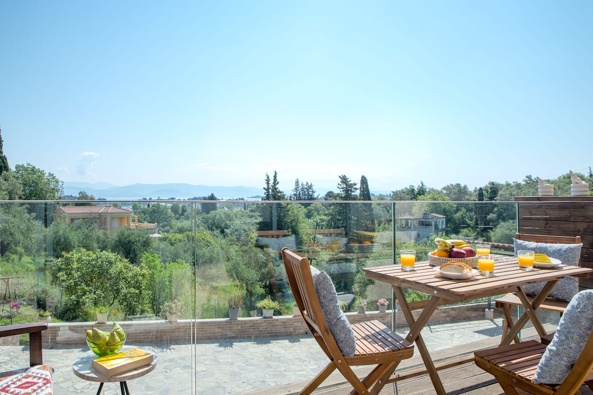 A wooden table with chairs on a balcony overlooking a scenic landscape.