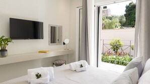 A hotel room with a bed, a TV, a small table with a plant, and a view of greenery outside. - Dimi Brou's Apartments by CorfuEscapes (Corfu)