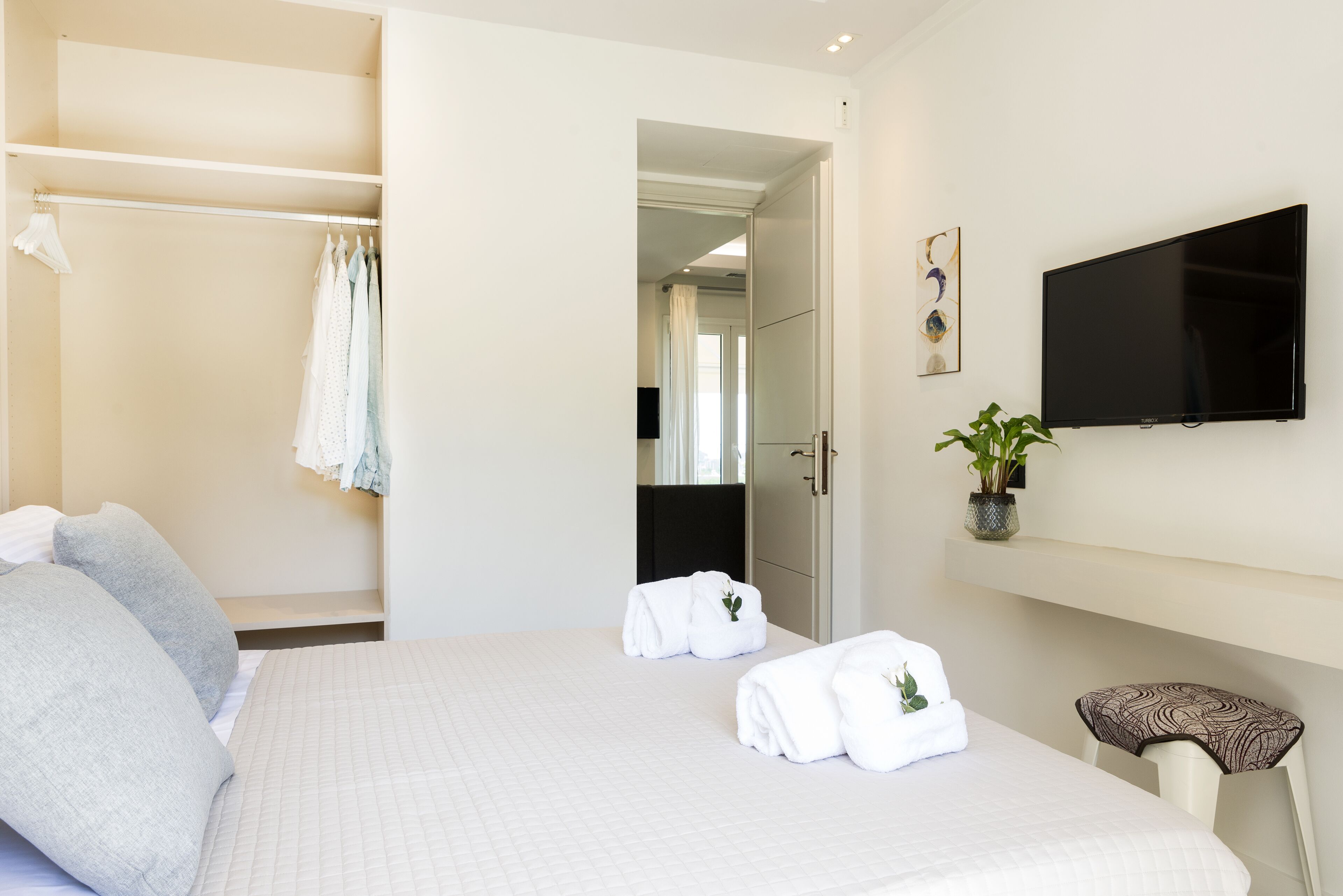 Quarto de hotel com cama, armário, televisão e planta em vaso.