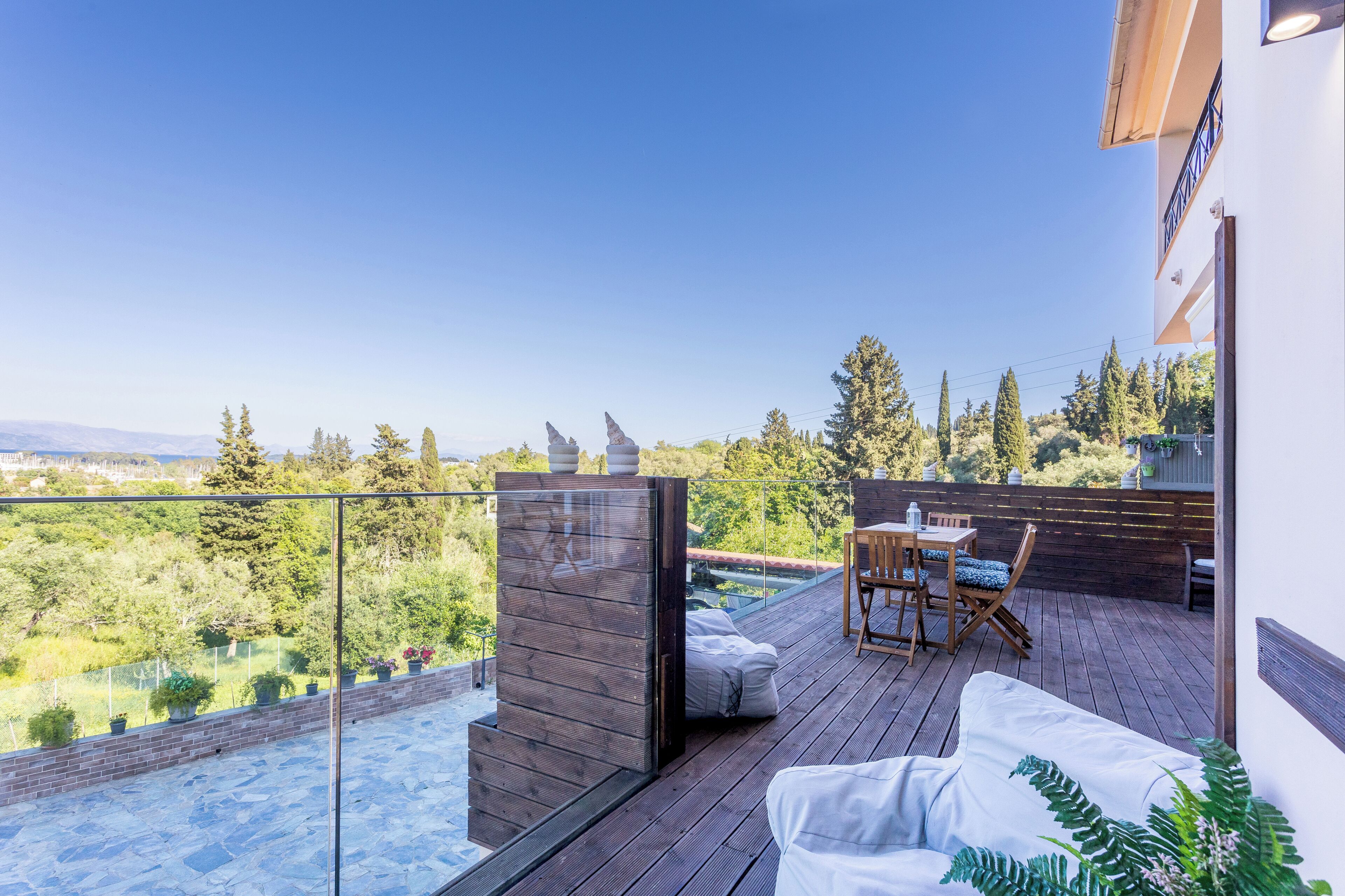 A wooden deck with a glass balustrade overlooking a garden and distant mountains.