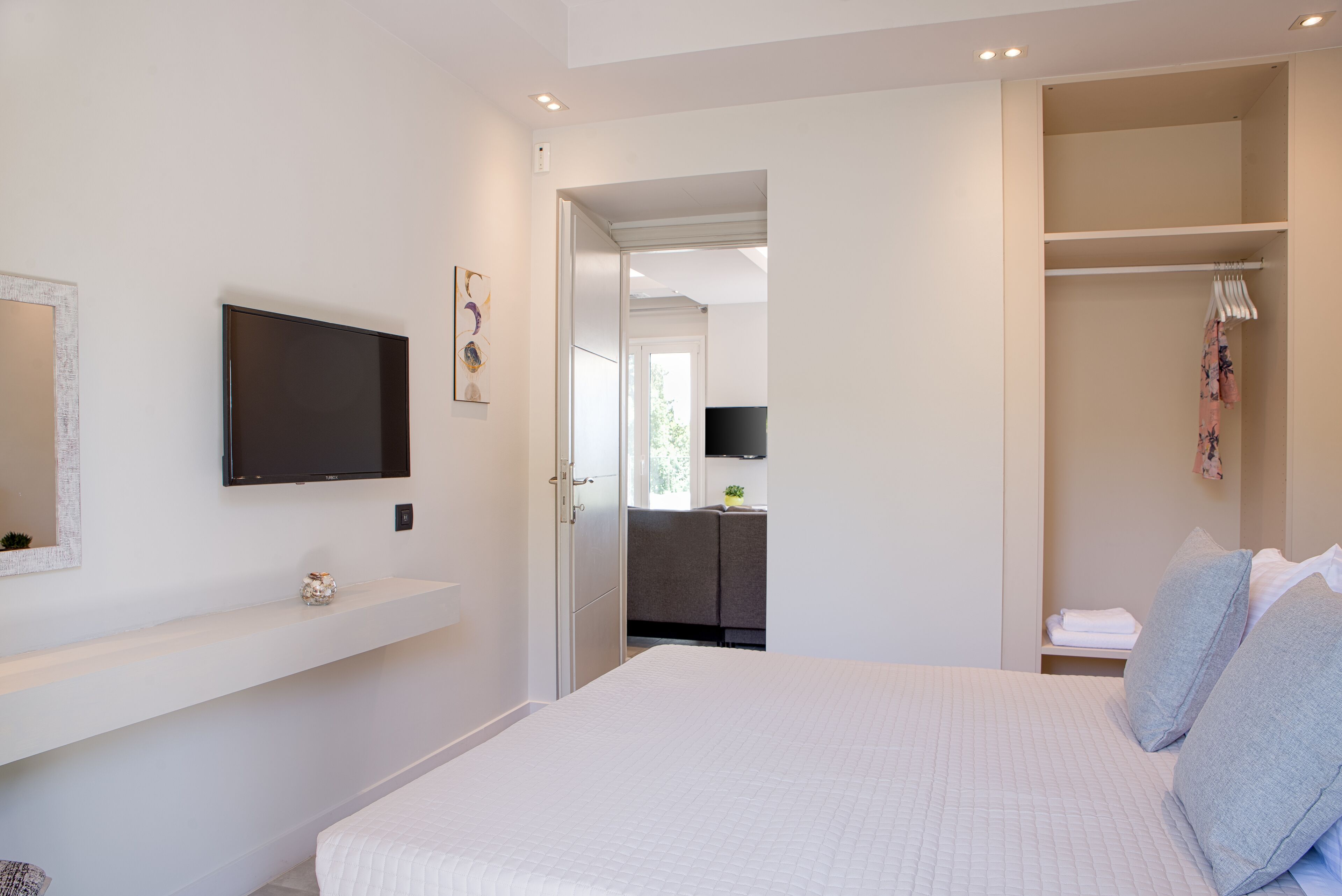 Une chambre à coucher comprenant un lit, un téléviseur fixé au mur, une armoire et un couloir menant à une salle de bain.