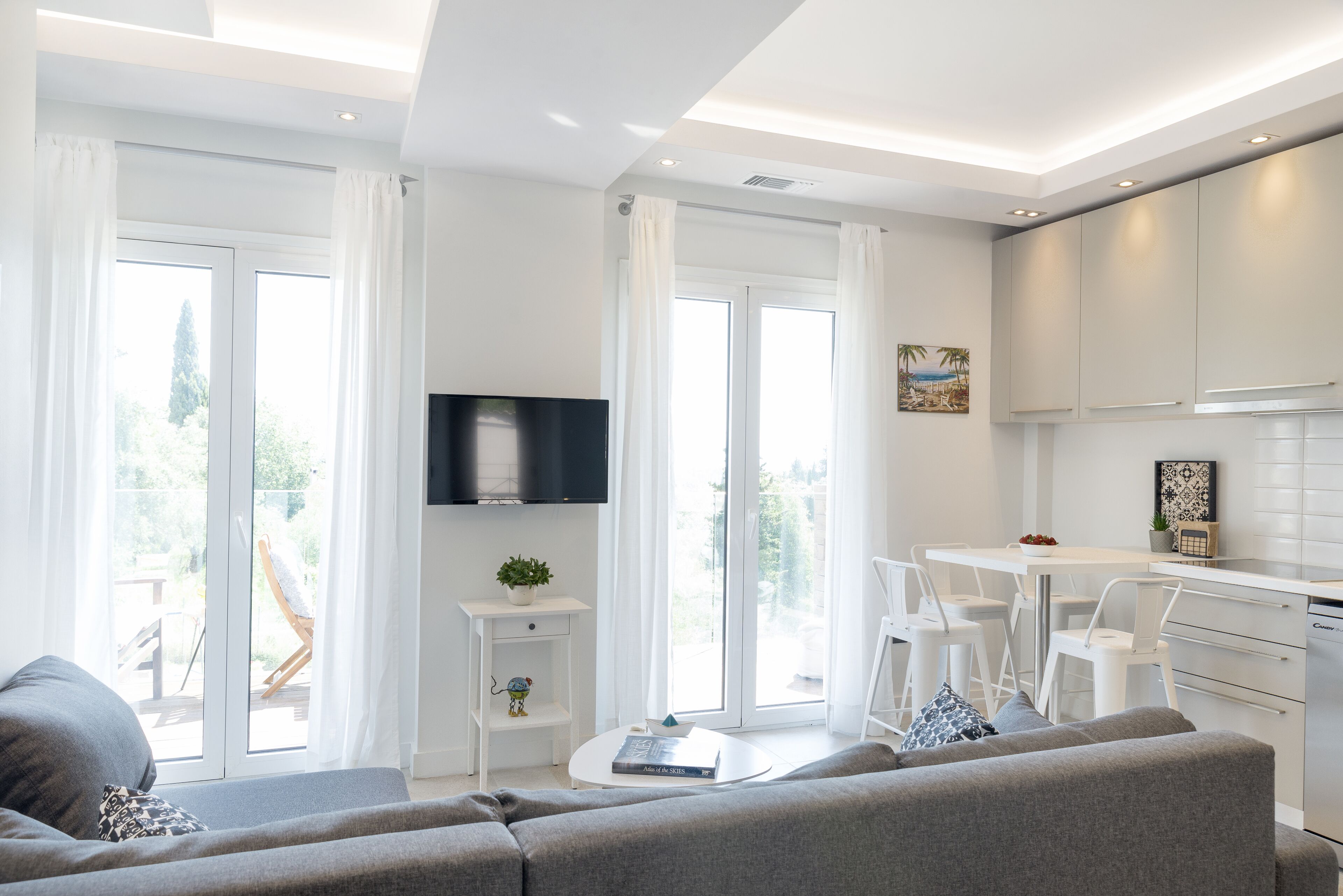 A modern living room with a grey sofa, a flat-screen TV, and a dining area with white chairs.