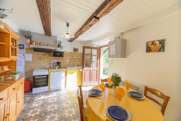 Una cocina con armarios de madera, un microondas y un lavamanos. Hay una mesa de comedor con platos y un florero.