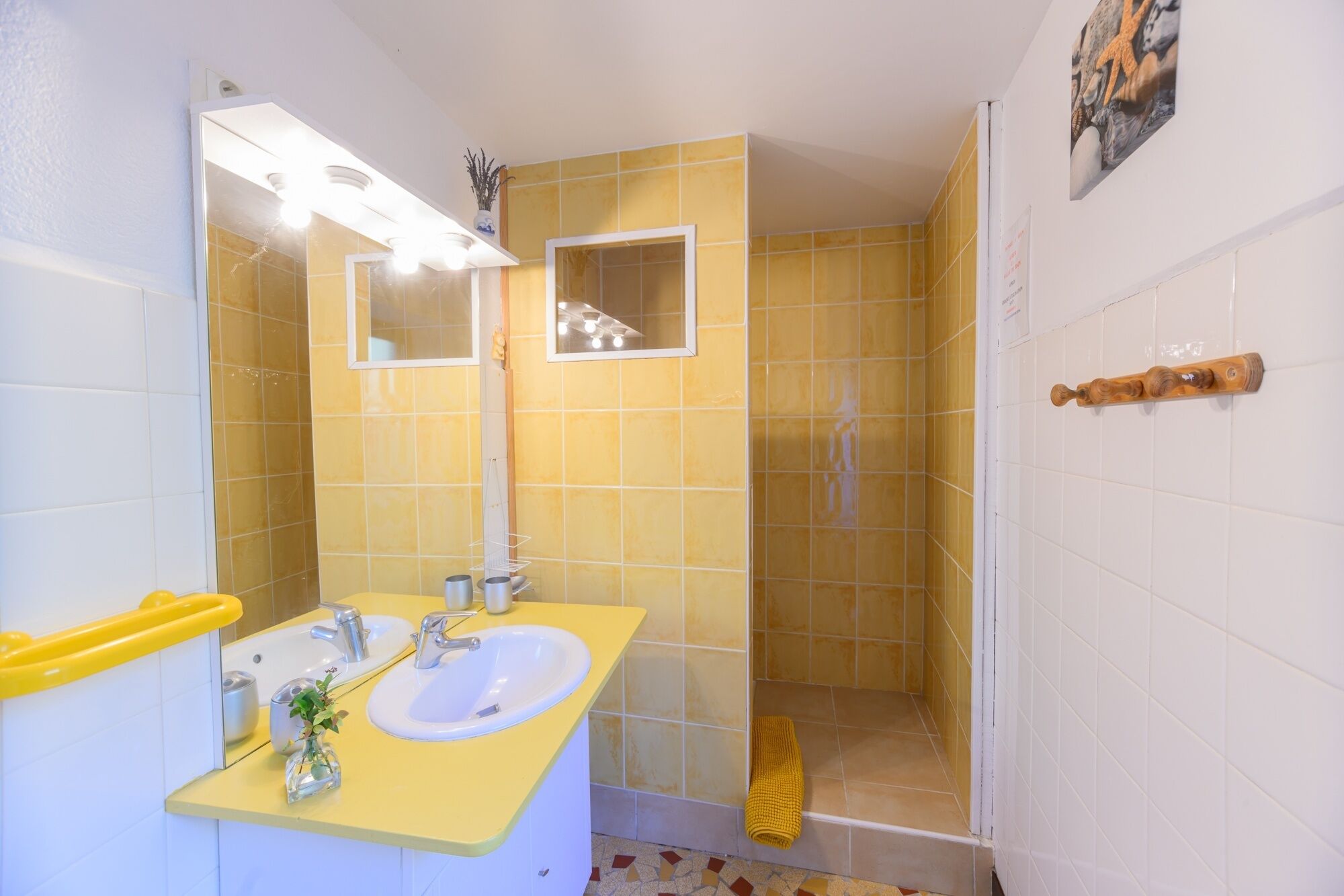 A bathroom with yellow tiles, a white sink, a mirror, and a shower area.