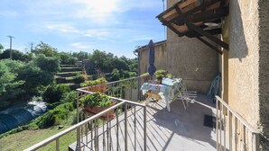 A balcony with a view of terraced fields, a table with chairs, and potted plants.