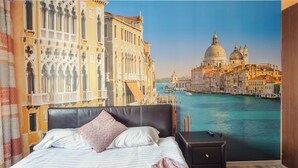 Een hotelkamer met een bed, een nachtkastje en een groot raam met uitzicht op de stad.