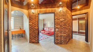 Een gang met een bakstenen muur, een rode leren bank en een eethoek met een tafel en stoelen.