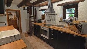 A kitchen with wooden beams, a large stove, and a window with a view of greenery. - RUSTIC BELLAVISTA (Caneggio)