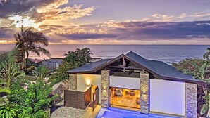 A modern house with a pool, surrounded by lush greenery and overlooking the ocean.