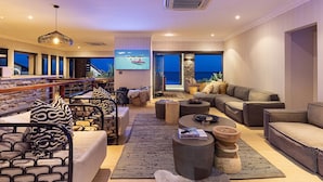 A modern living room with a large TV, comfortable seating, and a view of the ocean.