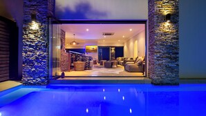A modern living room with a pool, stone walls, and a staircase leading to an upper level.