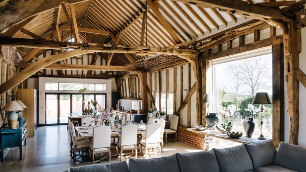Une pièce spacieuse avec des poutres apparentes, un coin repas comprenant des chaises et une table, et une grande fenêtre laissant entrer la lumière naturelle.