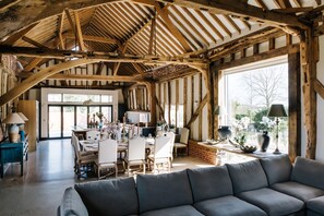 Una habitación amplia con vigas de madera a la vista, un comedor con sillas y una mesa, y un ventanal que proporciona luz natural.