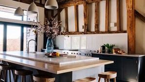 Une cuisine moderne dotée d’un grand îlot central, de tabourets de bar en bois, de luminaires suspendus et d’un plafond en bois au style rustique.