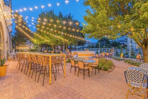 Un patio al aire libre con mesas, sillas, luces colgantes y árboles.