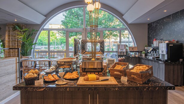 Un ricco buffet per la colazione con diversi cibi, una macchina per il caffè e un'ampia finestra vista alberi.